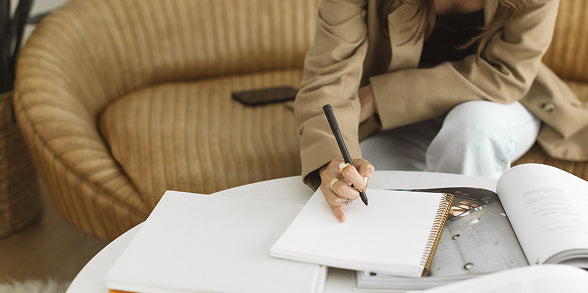 Person sitting on a couch writing in a notebook with a pen.