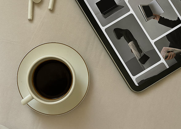 Coffee cup on a saucer next to a tablet displaying images of people working.