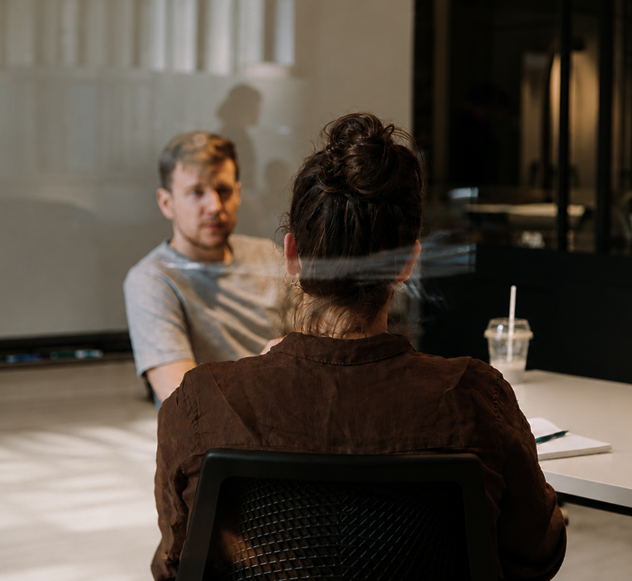 Two people sitting across from each other in a room with a screen in the background