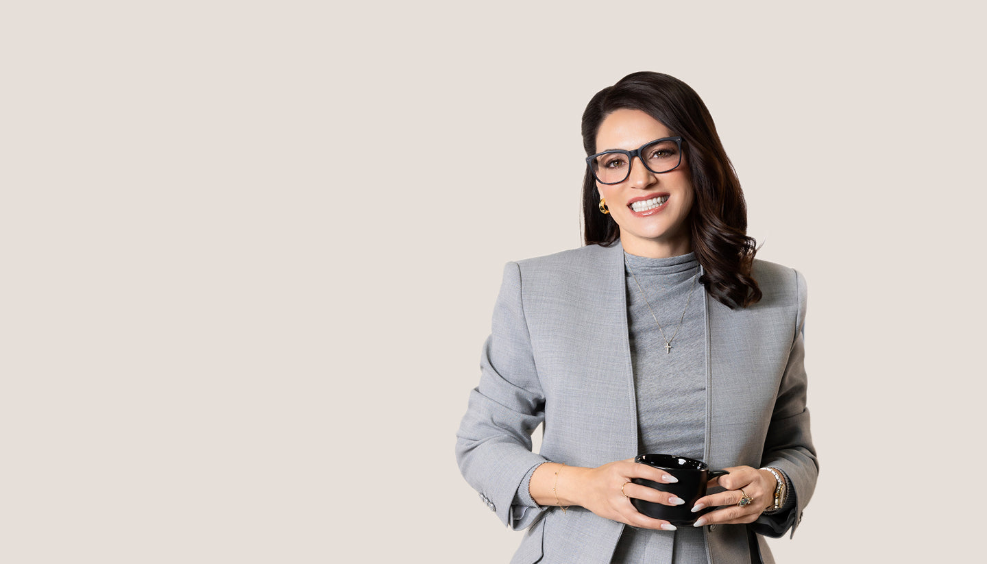 Woman in a gray suit holding a phone against a beige background