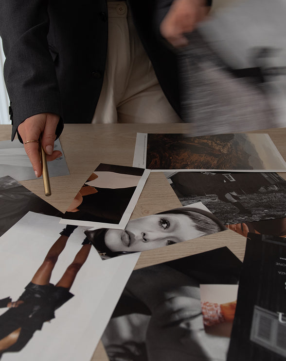 Person holding a gold pen over a collage of black and white photos on a table.