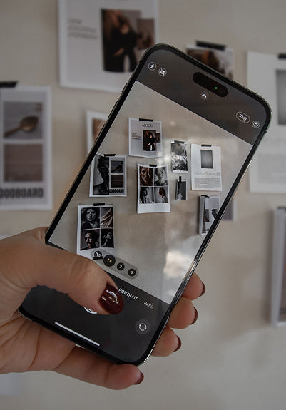 Hand holding a smartphone taking a photo of a wall with black and white photos.