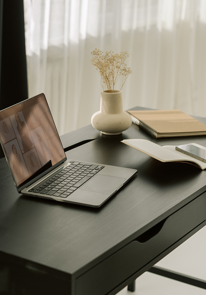 Laptop on a desk with a vase and notebook in the background