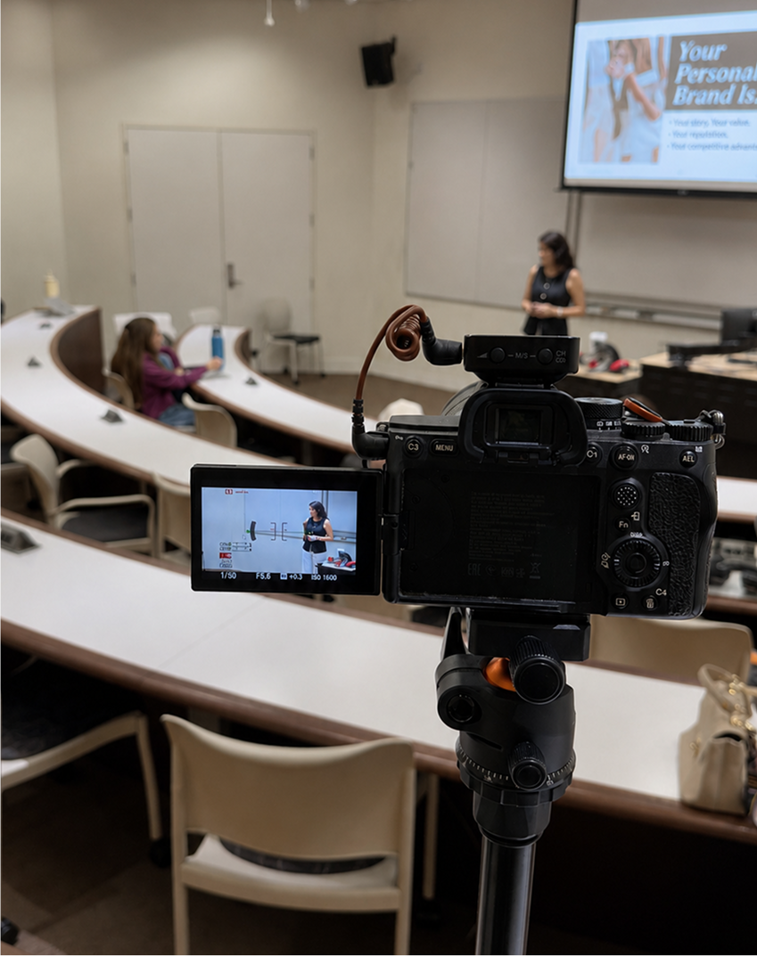 Camera on a tripod recording a classroom setting with a screen displaying a presentation.